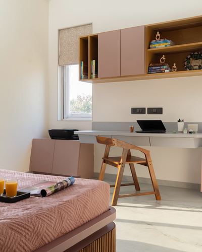 Sunlit study nook with pink cabinetry, wooden chair, desk with laptop, and marble floor.