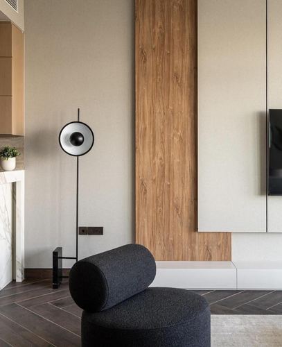Minimalist living room corner with wood panel, black floor lamp, and dark bolster ottoman