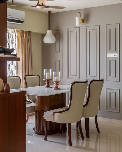 Dining room with marble-top table, wingback chairs, and paneled taupe wall with sconce