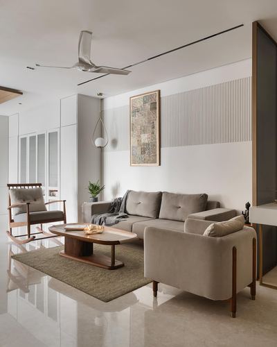 Minimalist living room with beige sofas, wooden rocking chair, and ribbed accent wall in Chennai apartment