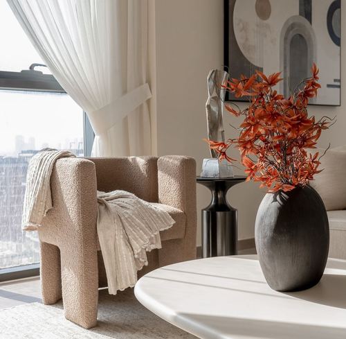 Beige boucle armchair by window with throws, dark vase of orange branches on round table