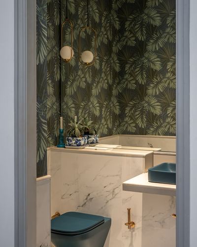 Powder room with palm-print wallpaper, marble counter, teal sink and toilet, brass pendant lights