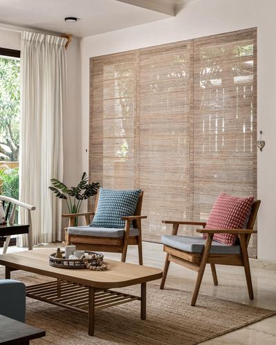 Living room with two teak armchairs, blue and red cushions, facing a large woven cane screen with garden light behind.