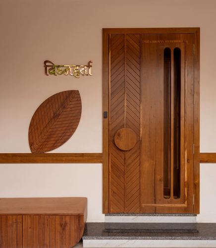 Wooden chevron-patterned front door beside a carved leaf-shaped wall panel and nameplate in a foyer