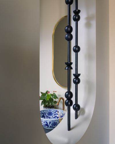 Blue and white ceramic vessel sink with brass tap seen through an arched cutout hung with black turned-wood bead chains.