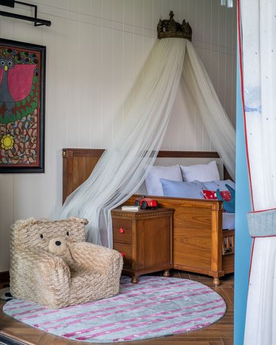 Child's wooden bed with sheer canopy under carved crown, teddy bear armchair, folk art on wall
