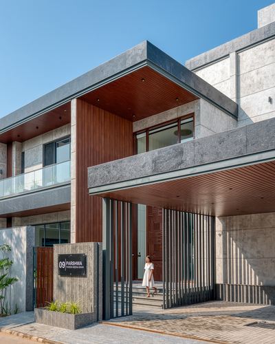Contemporary stone villa facade with wood-lined cantilevered entry canopy and vertical metal louvers, woman standing at steps