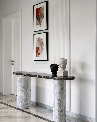 Marble console with cylindrical legs beneath framed art and sculptural busts in a foyer