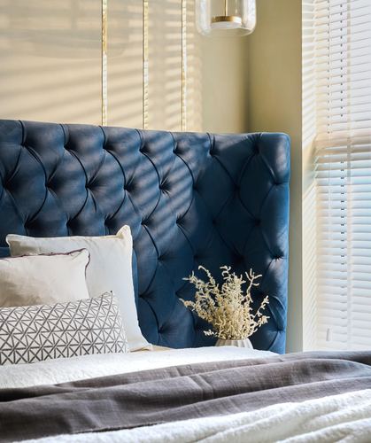 Navy tufted velvet headboard beside sunlit blinds with layered gray and white bedding