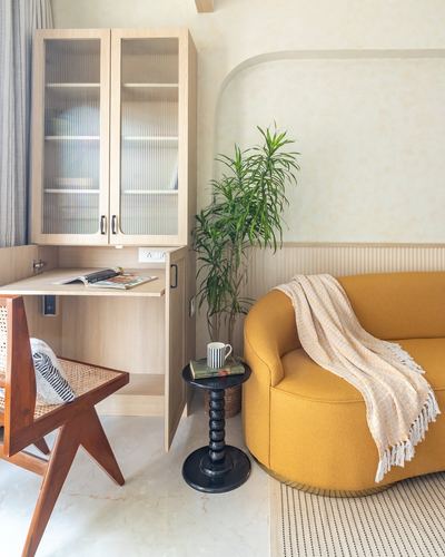 Living room corner with mustard curved sofa, cane chair, ribbed wood cabinet and indoor plant