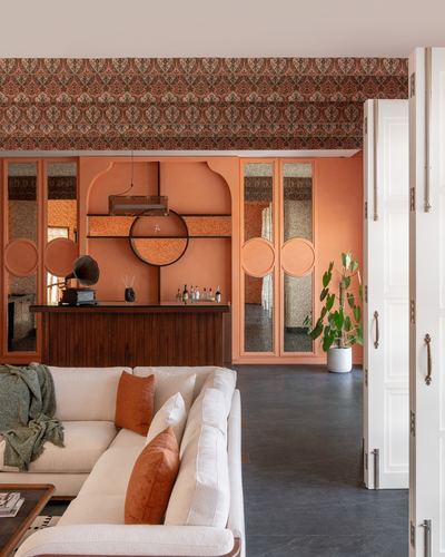 Terracotta-toned living room with bar niche, round mirror, and cream sectional sofa