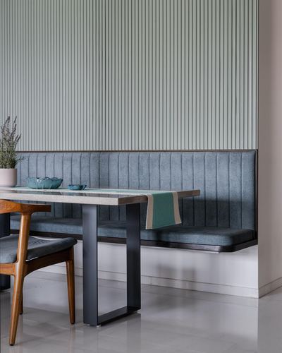 Fluted green wall panel above a channel-tufted blue-grey banquette with a marble-top table
