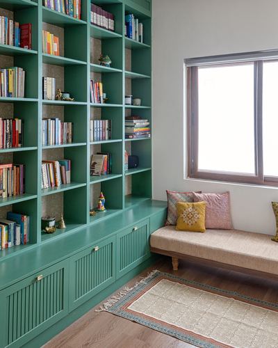 Teal built-in bookshelf beside a cushioned window bench with patterned rug on wood floor