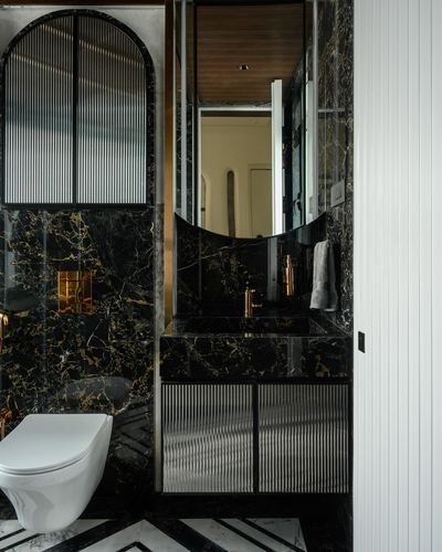 Dark marble powder room with arched fluted door, curved mirror, and brass fixtures
