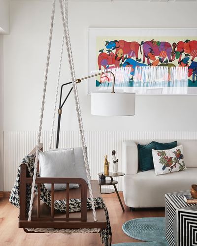 Living room corner with wooden hanging swing, arc lamp, and folk art print above sofa