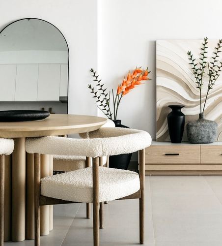 Round wood dining table with boucle chairs beside an arched mirror and textured console vignette