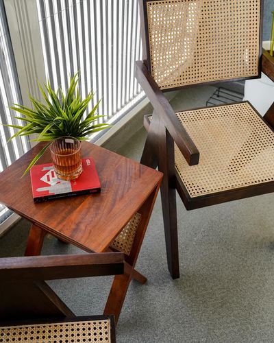 Cane armchair beside wooden side table with plant and drink near louvered window