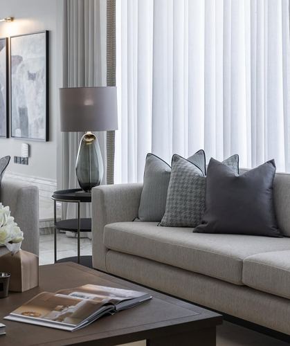 Neutral living room with grey sofa, patterned pillows, glass table lamp, and sheer curtained window