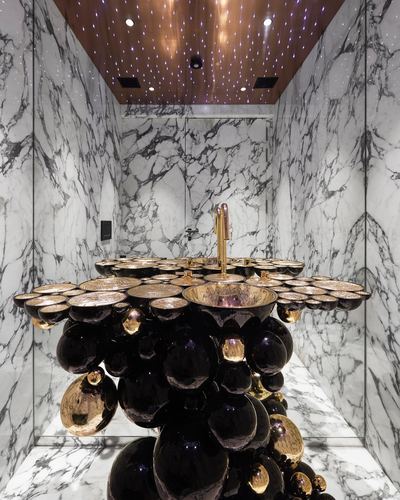 Marble bathroom with a sculptural black and gold spherical sink pedestal under a starlit ceiling