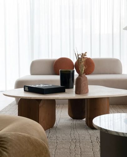Beige sofa with terracotta round cushions behind an oval stone coffee table on wooden legs