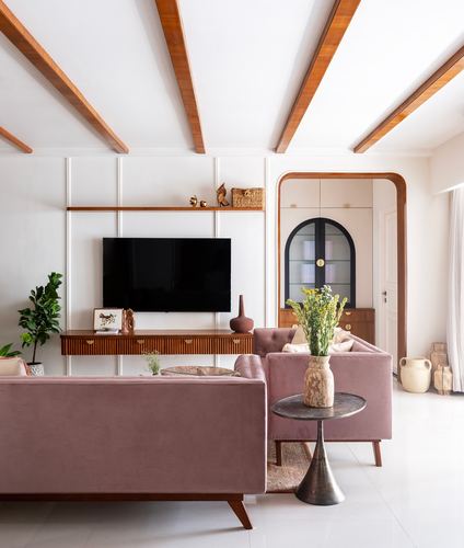 Living room with pink velvet sofas, wooden beamed ceiling, and an arched glass cabinet in the background