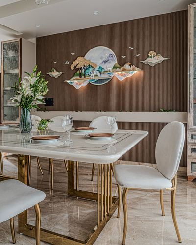 Dining table with brass legs set before a fluted brown wall with sculptural mural