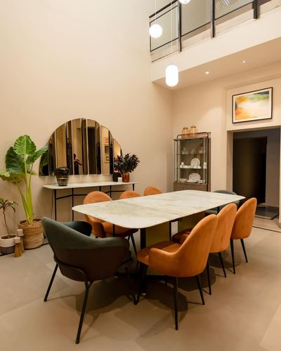 Double-height dining room with marble table, orange and green velvet chairs, arched mirror on wall