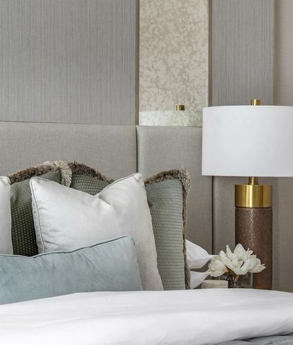 Close-up of upholstered bed with layered pillows beside a brass table lamp and panelled wall