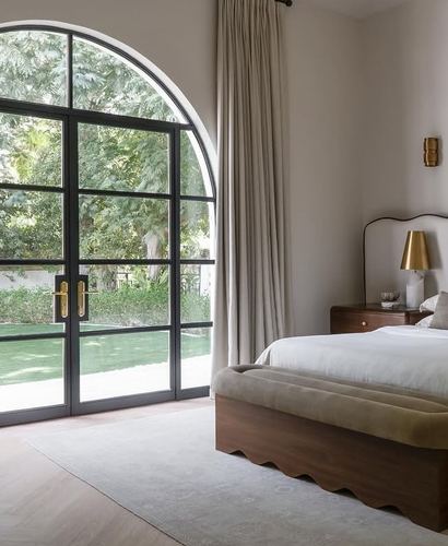 Bedroom with arched black steel doors opening to garden, curved headboard bed and scalloped bench