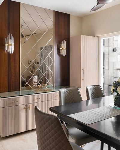 Art deco dining room with mirrored diamond wall, fluted pink cabinetry, and black table with quilted chairs