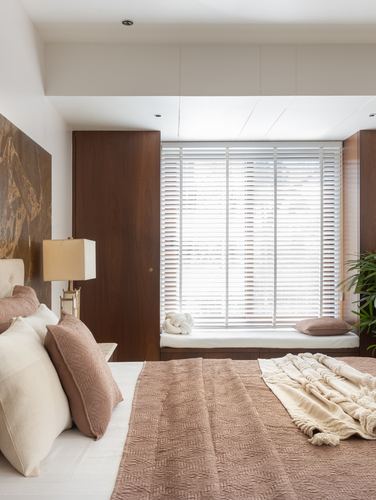 Bedroom with wood wardrobes, window seat with slatted blinds, and bed with rose-toned linens