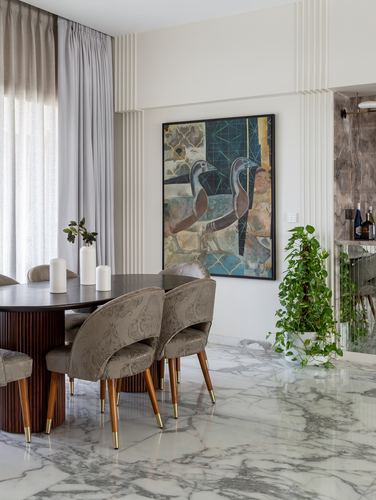 Dining table with fluted base and patterned chairs beside a bird artwork on marble floor