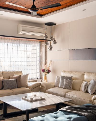 Cream leather sofas around marble coffee table beneath wood ceiling and hanging glass pendants
