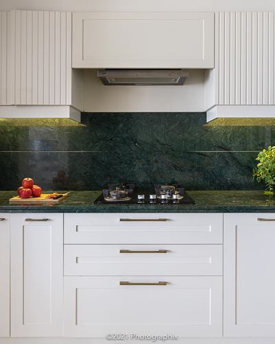 White fluted-panel kitchen with green stone backsplash, gas hob, chimney hood, and brass handles
