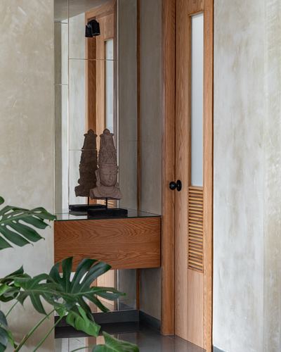 Foyer with wooden console, mirror, stone bust, and louvered wooden door beside plaster wall