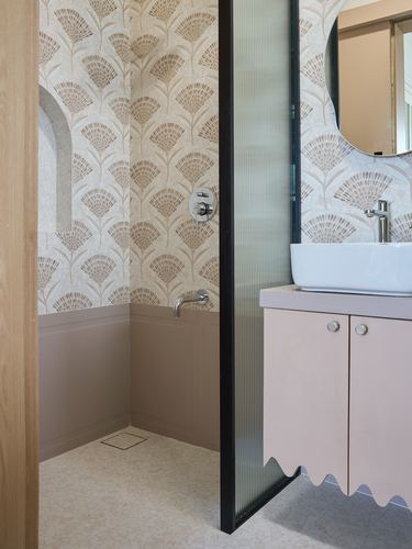Pink bathroom with patterned wallpaper, terrazzo floor, and reeded glass partition wall