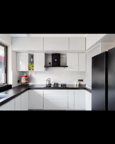 White glossy L-shaped kitchen with black countertop, hood, and matte black refrigerator