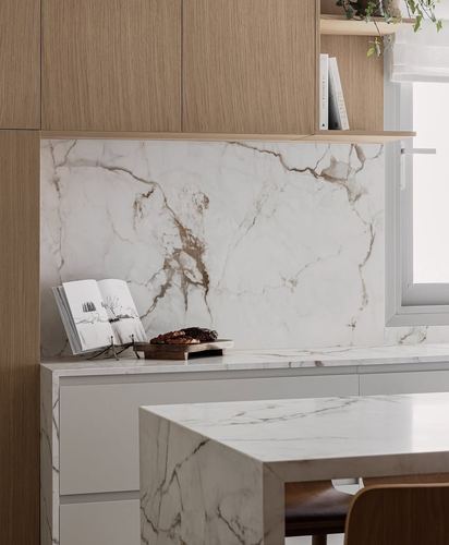 Kitchen corner with marble-look stone backsplash, wood cabinetry, and a waterfall-edge island under a window