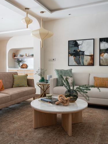 Living room with beige sofas, round marble-top coffee table, and sculptural gold pendant lights