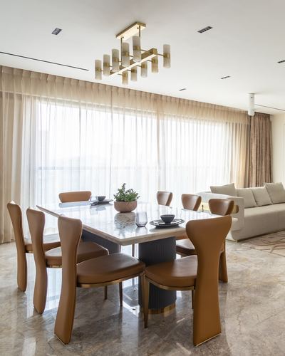 Dining room with marble table, camel leather chairs and brass chandelier against sheer-curtained window