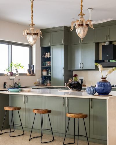 Olive green kitchen island with ornate glass pendant lights and a cat on the counter
