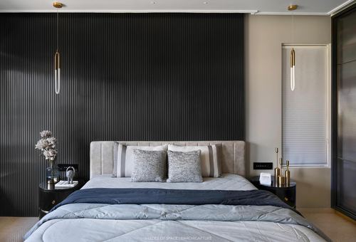 Bedroom with fluted dark panel wall, upholstered bed, brass pendant lights on either side