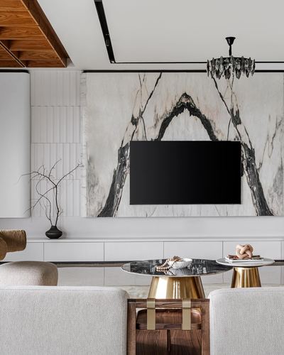 Living room with bookmatched marble tv wall, brass-legged round tables, and beige sofas