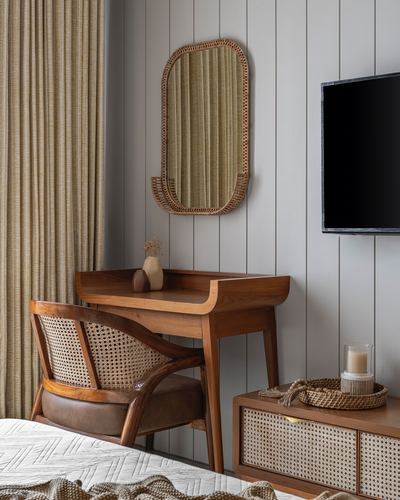 Wooden desk and cane chair beneath a rattan-framed mirror against panelled grey wall