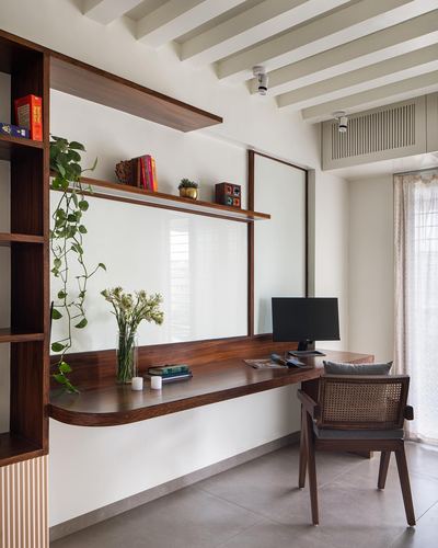 Wooden study nook with floating curved desk, cane chair, and trailing plant under mirrored shelf
