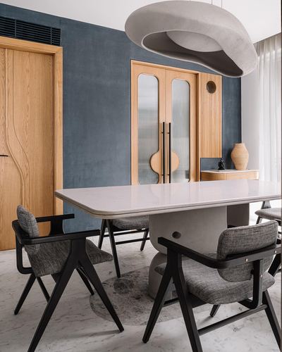 Dining room with sculptural pendant light over marble table and black chairs against a blue wall