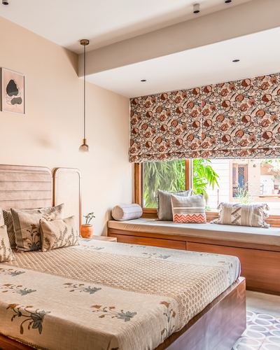 Bedroom with wooden bed, floral roman blind, and window seat overlooking greenery
