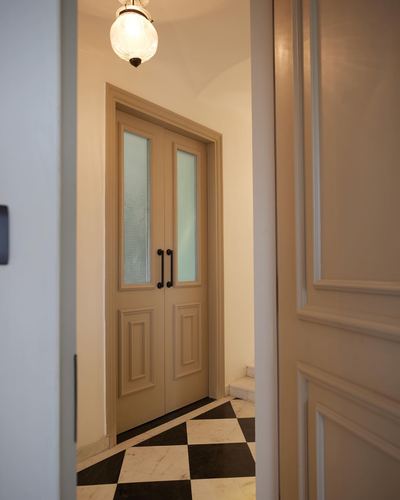Beige double doors with frosted glass panels seen through an open door onto a black and white checkerboard marble floor