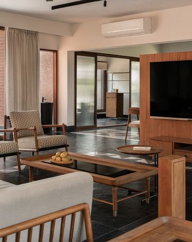Living room with wooden furniture, patterned stone floor, and glass partition to inner room