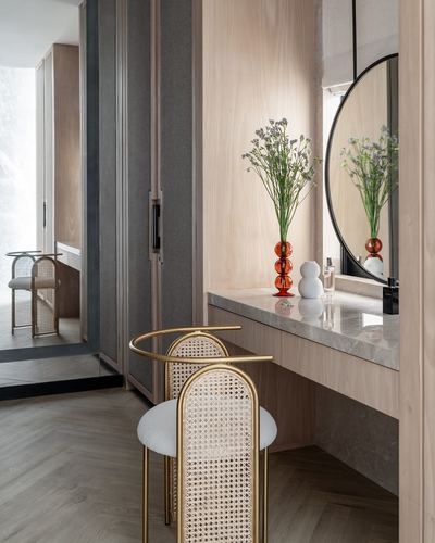 Wood-panelled dressing vanity with round mirror, marble counter, and cane stools in a herringbone-floored corridor